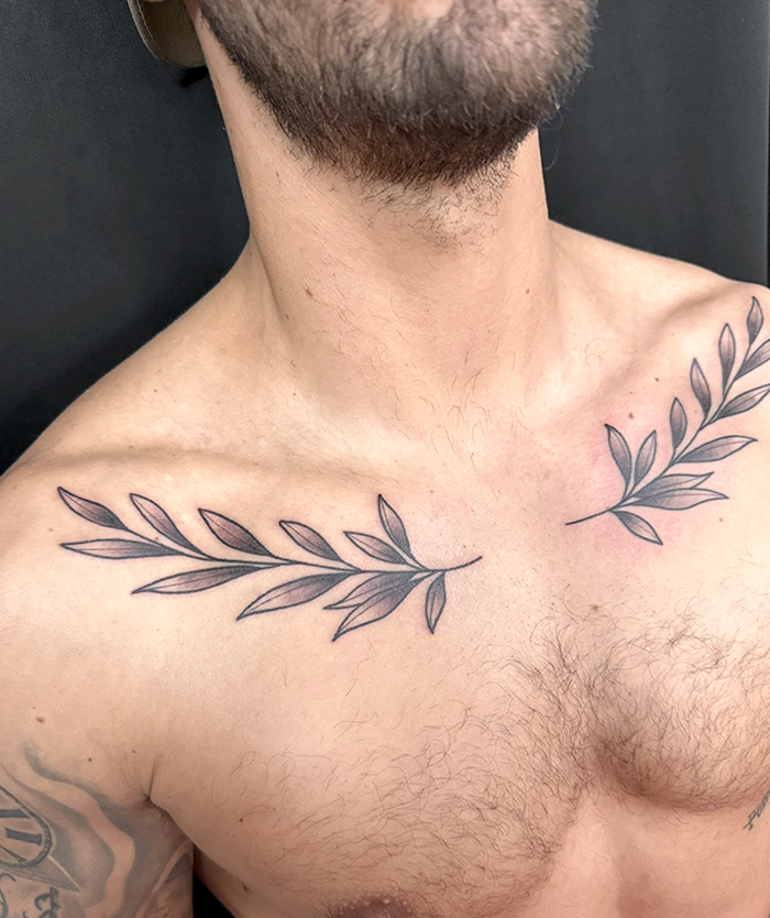 Tatoeage van twee takken met bladeren op de schouders van een man zonder shirt.
