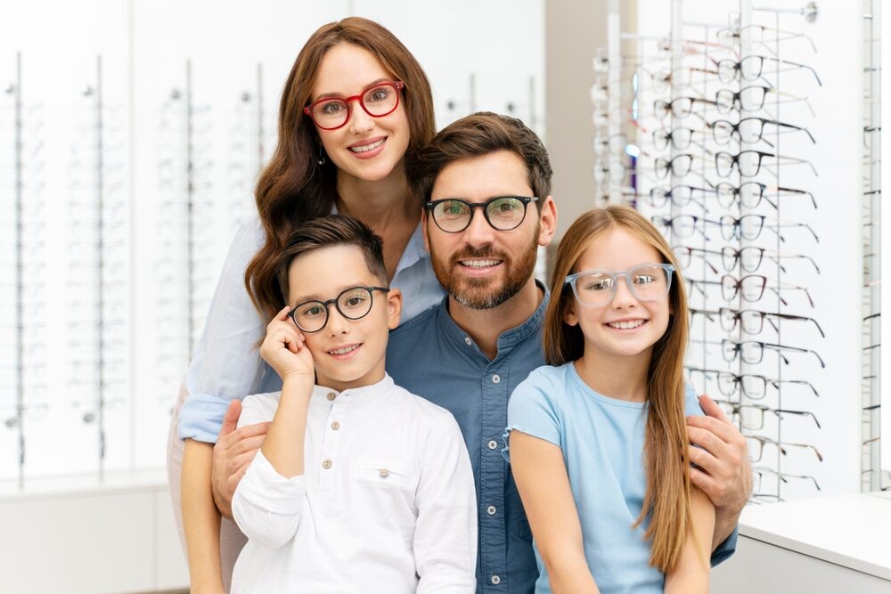 See the Good: Help Us Fill Backpacks for the Boys and Girls Club This Summer!  Portrait of young smiling family hugging choosing stylish glasses in modern optical store. Vision concept .