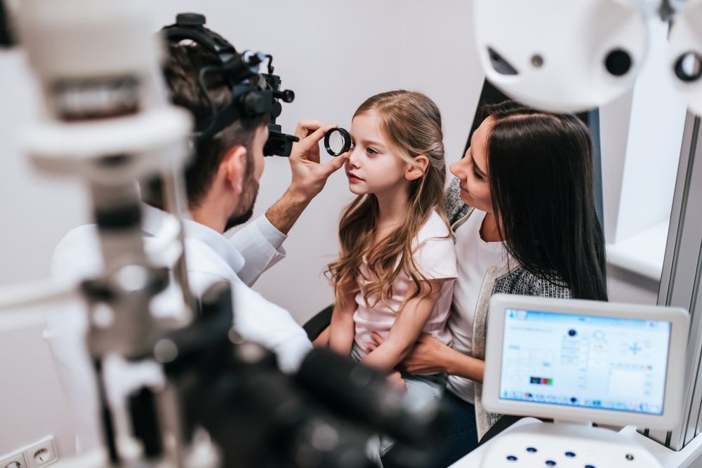 Myopia Control Techniques? male eye doctor is checking the eye vision of little cute girl in modern clinic.