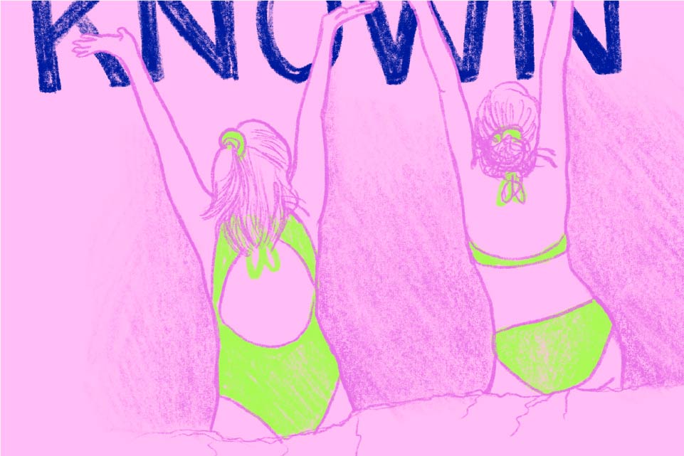 2 women standing in the ocean in bikini with back towards viewer