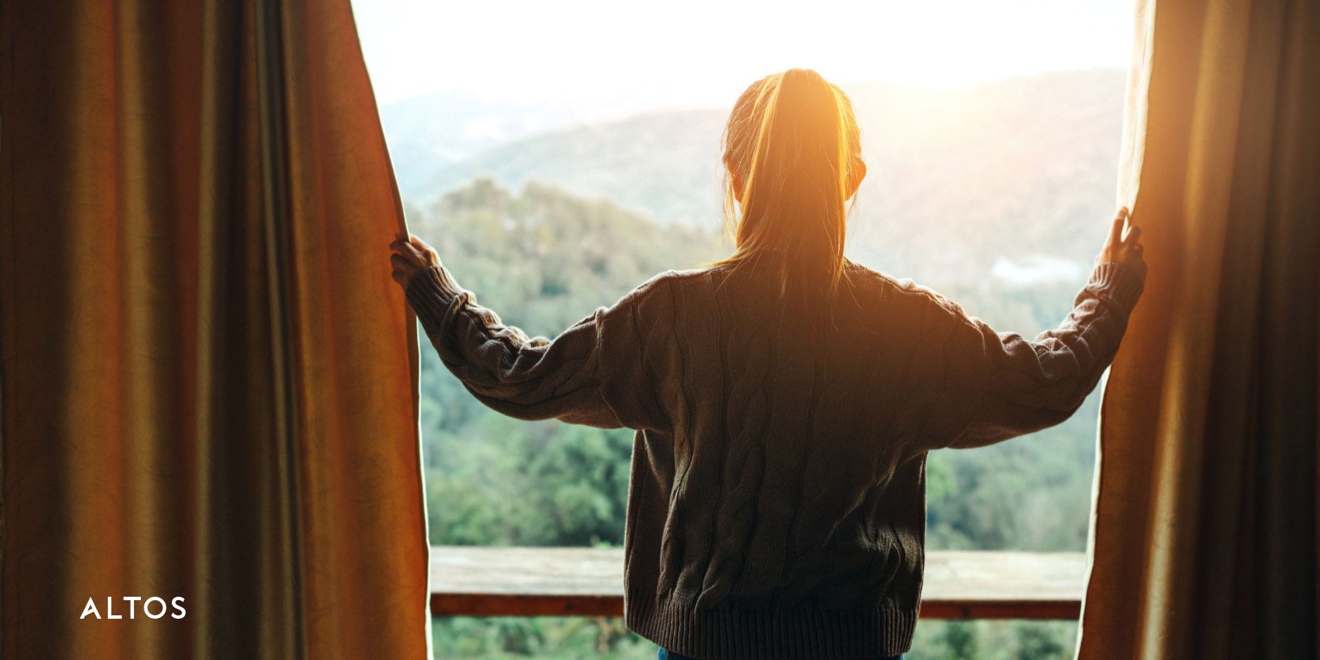 Traveler opening the curtains in her hotel room, revealing a mountain view on a sunny day.