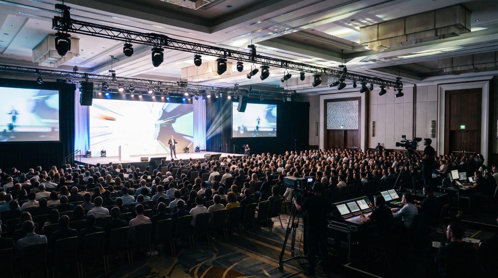 Audience seated at a corporate conference general session with a speaker on stage and a large LED screen