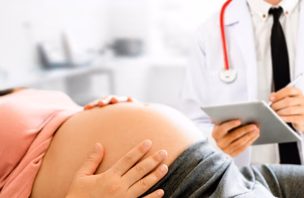 Closeup of a pregnant woman's bare belly with her OBGYN in the rear, blurred out of focus. Doctor errors can lead to common birth injuries.
