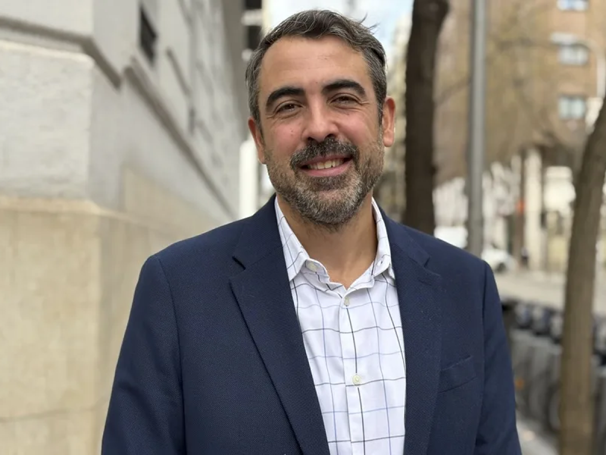Man smiling outdoors on a city street, wearing a blazer and button down shirt.