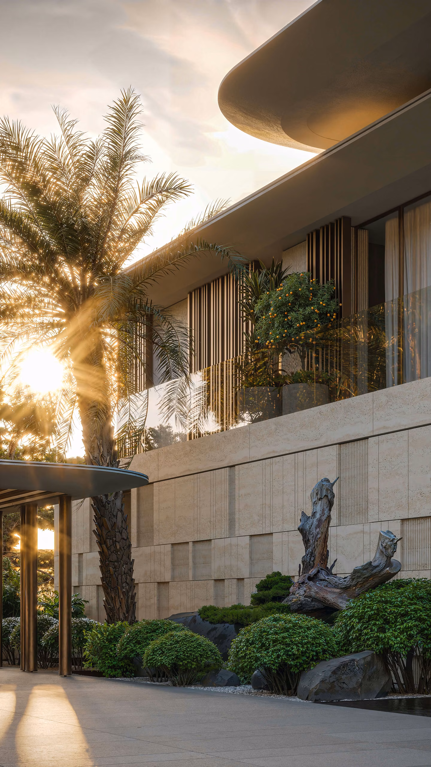 Entrance detail with a stone facade, curved roof and palms lit by the low sun.