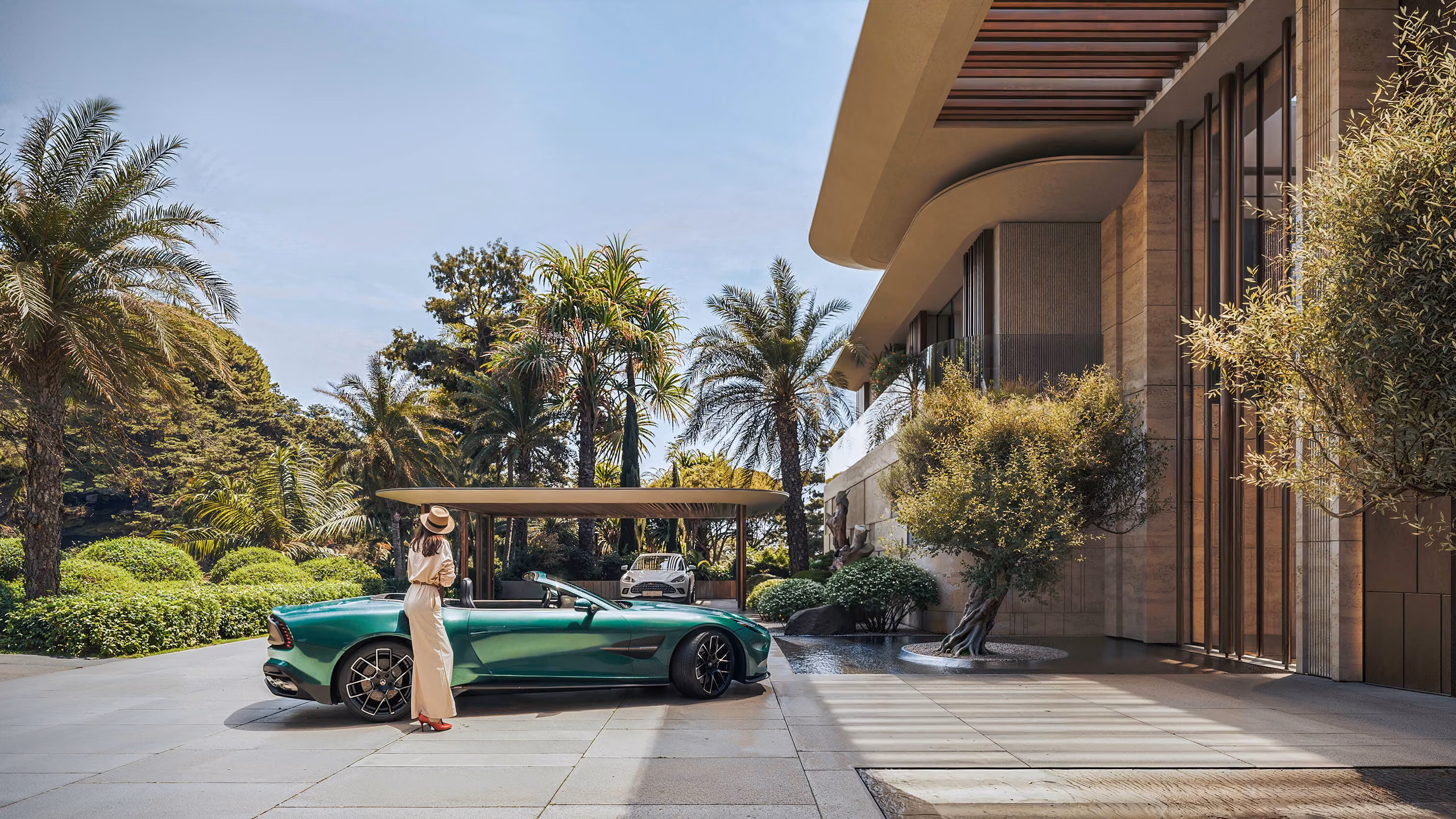 Entrance courtyard with a green convertible, a figure beside the car and a palm garden.