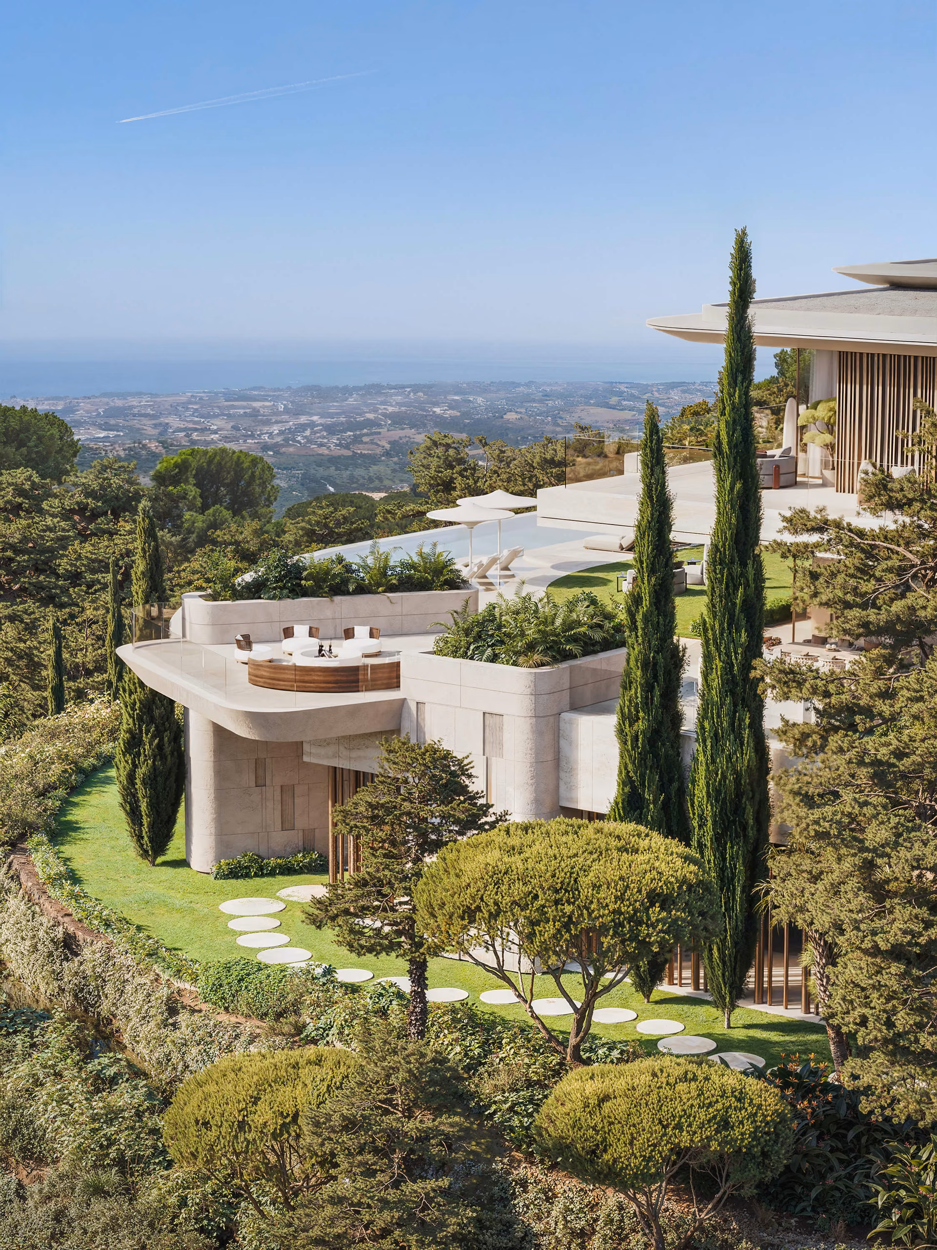 Stepped terraces and garden on the hillside, with cypresses and open coastal views.