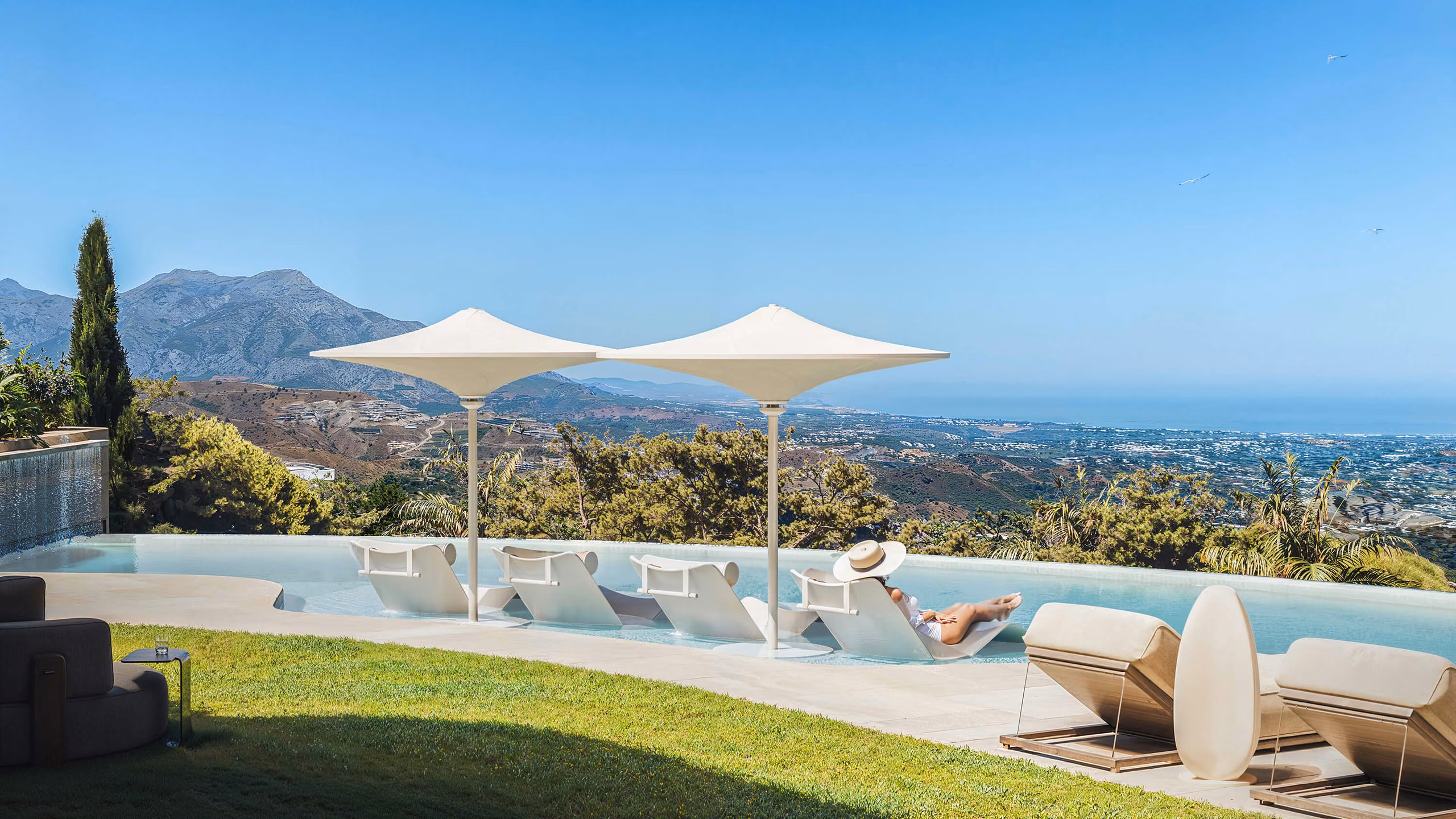 Loungers and white parasols beside the pool, overlooking the mountains and coast.