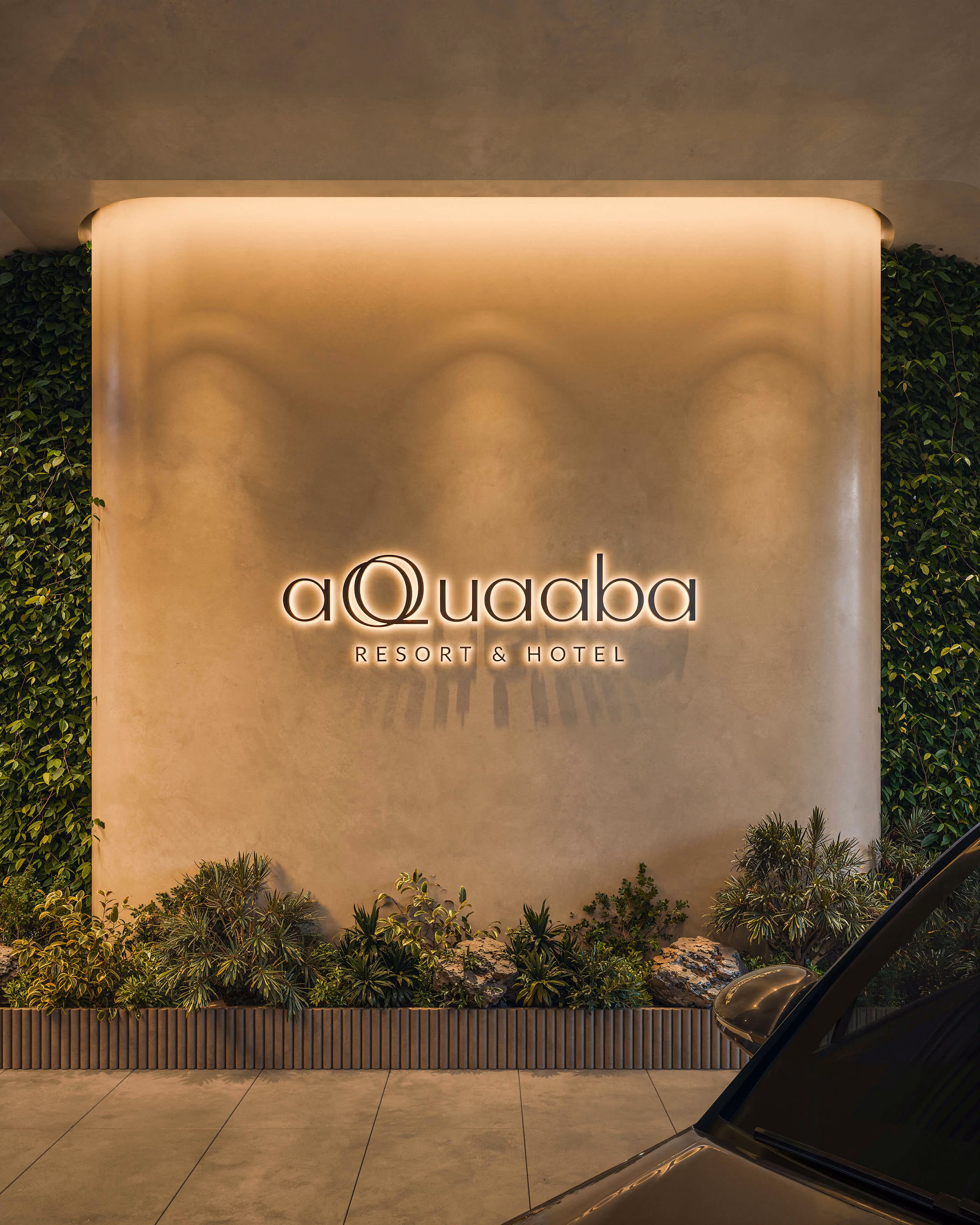 Illuminated Aqquaaba Resort Hotel sign on a curved wall with planting at its base.