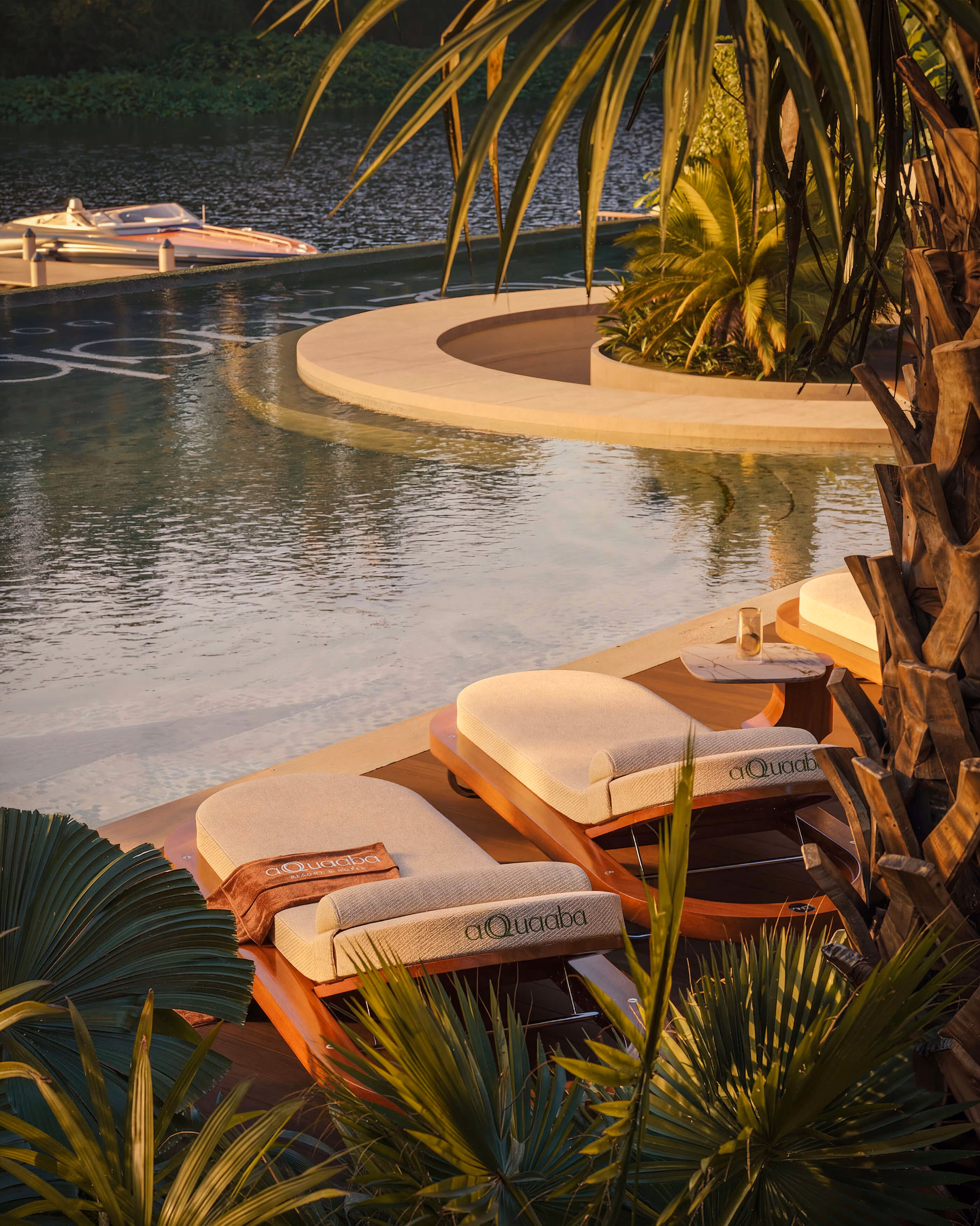 Two loungers beside the curved edge of the Aqquaaba pool among palms in warm light.