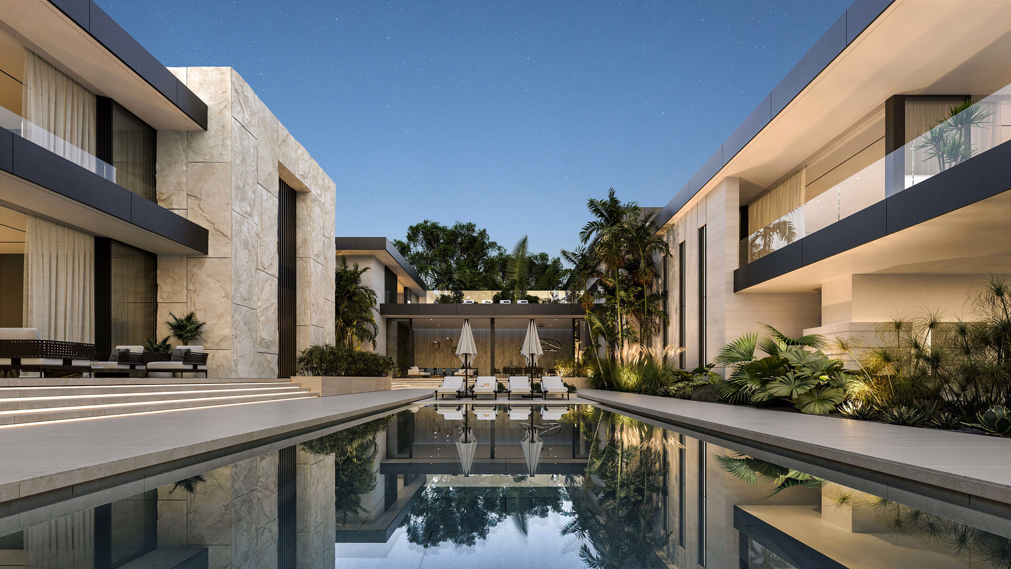 Piscina entre dos alas de la vivienda, con terrazas iluminadas y tumbonas al fondo.