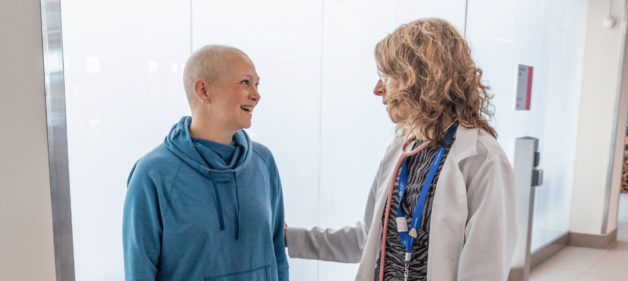 一名乳腺癌患者在医院走廊里与肿瘤科医生交谈时展露笑容，治疗期间共享着这段互勉互慰的温馨时刻。