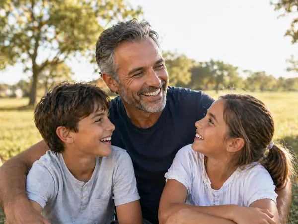 Smiling father sitting outdoors with his son and daughter, all looking at each other happily with concierge primary care medicine