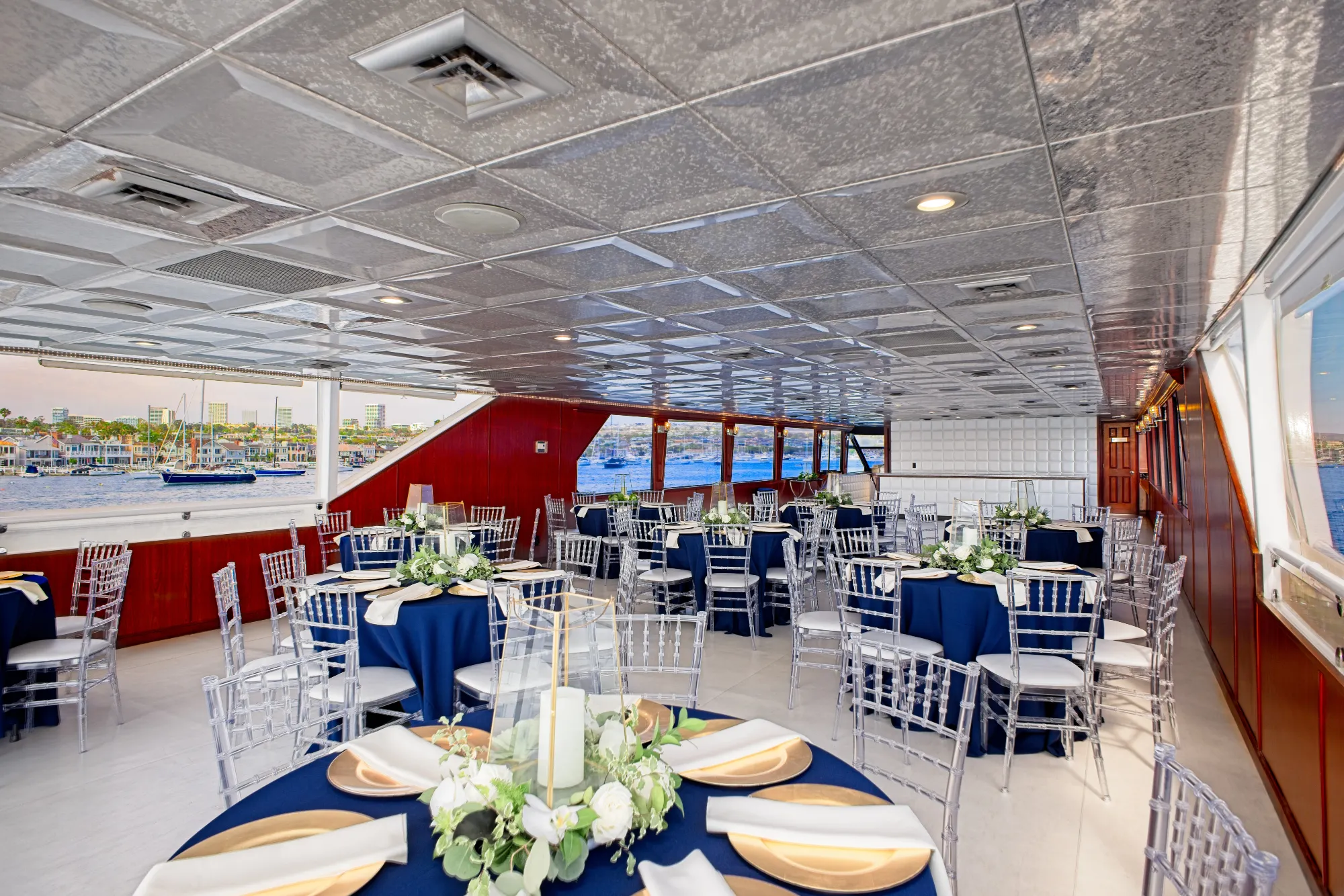 Elegant boat dining area with navy tablecloths, clear chairs, floral centerpieces, and waterfront views.