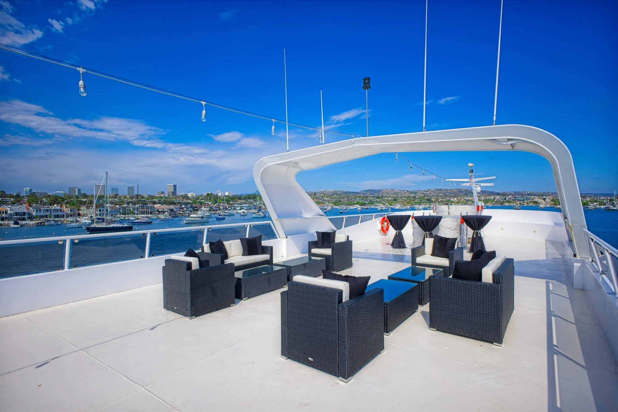 Modern outdoor lounge seating on a yacht deck with a harbor and city skyline in the background.
