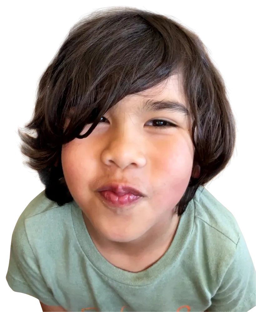 Close-up of a young child with dark hair smiling slightly and wearing a green shirt.