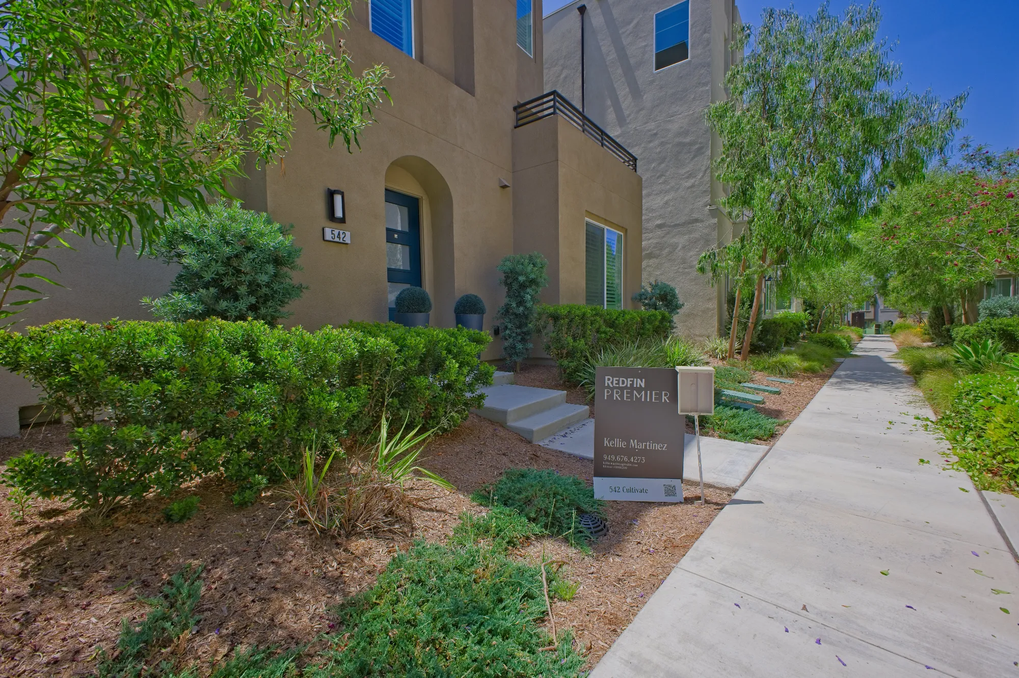 Modern townhouse entrance with greenery, pathway, and a Redfin Premier real estate sign.