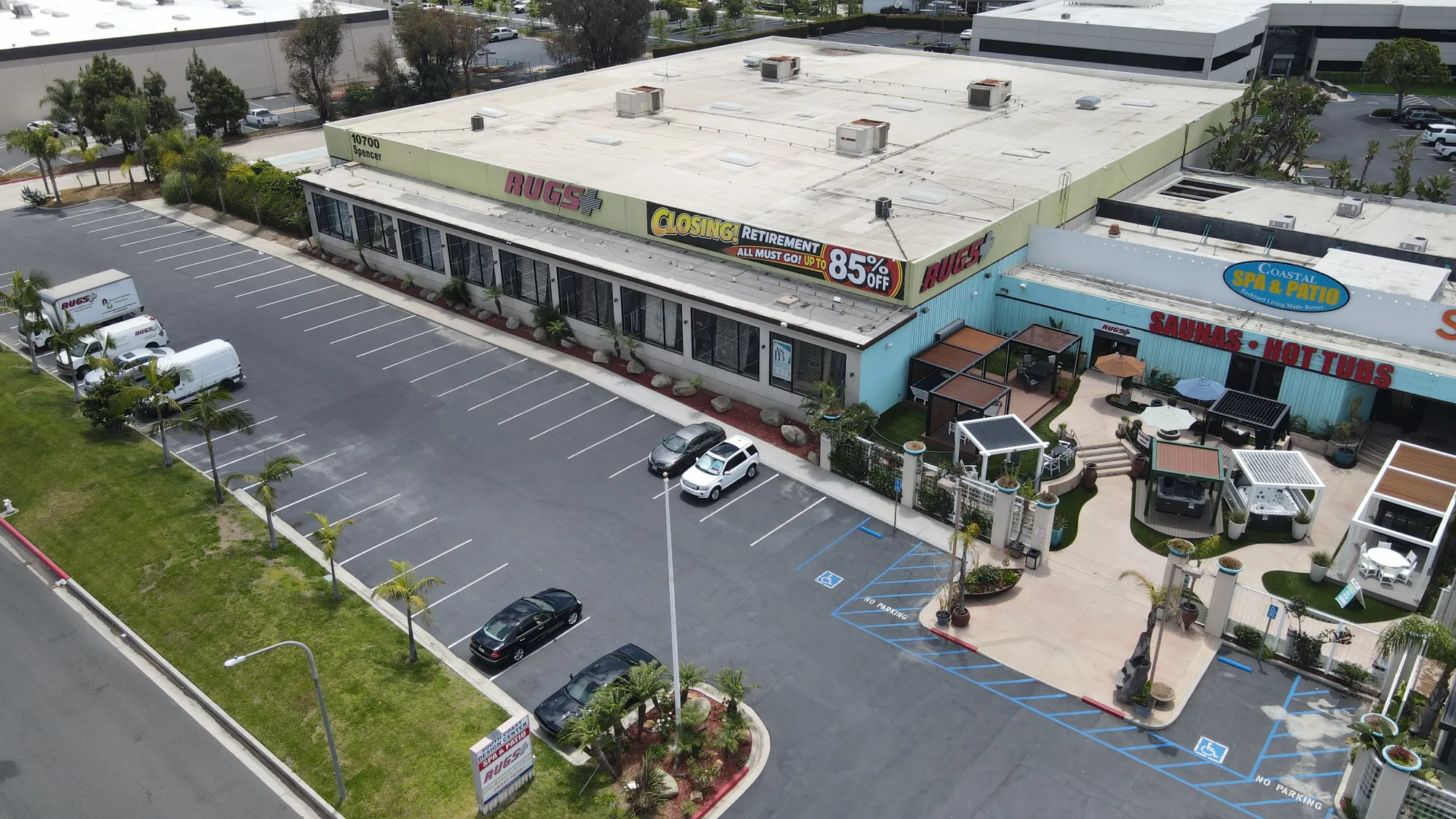 Aerial view of a building with Rugs Plus store closing sign and adjacent Coastal Spa & Patio showroom outdoors.