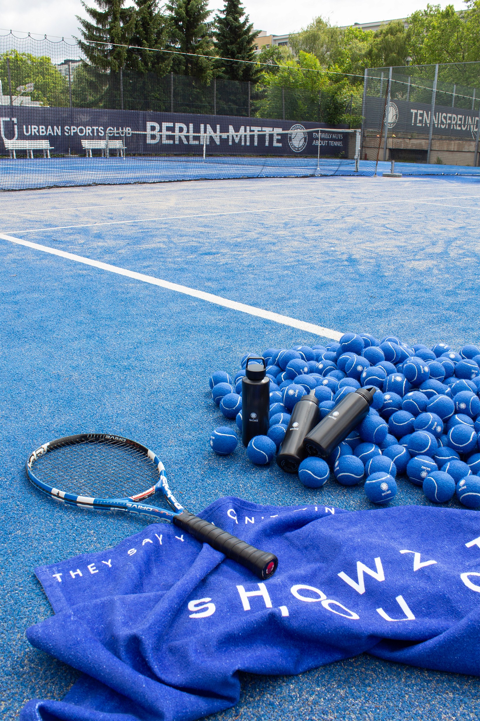 Tennisfreunde x SHOWZ: tennis court styled with a SHOWZ towel, racket and blue tennis balls