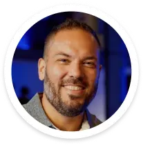 Smiling man with short hair and beard wearing a light-colored shirt against a blue background.