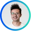 Smiling man with curly hair and glasses inside a blue circular frame on a white background.