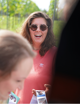 Mitarbeiterin mit Sonnenbrille lacht und hält Fotos bei einem Sommerfest der Agentur.
