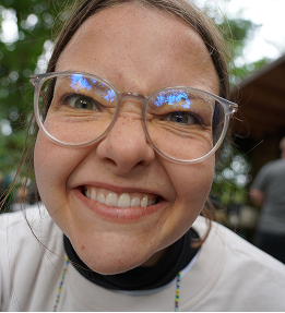Nahaufnahme einer lachenden Mitarbeiterin mit Brille bei einem Outdoor-Event.