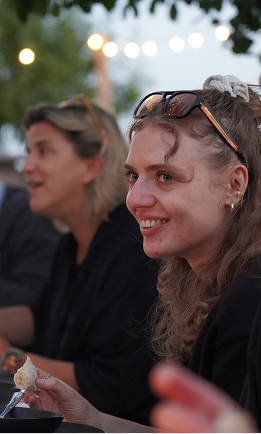 Lachende Mitarbeiterin sitzt beim Agentur-Sommerfest draußen am Tisch.