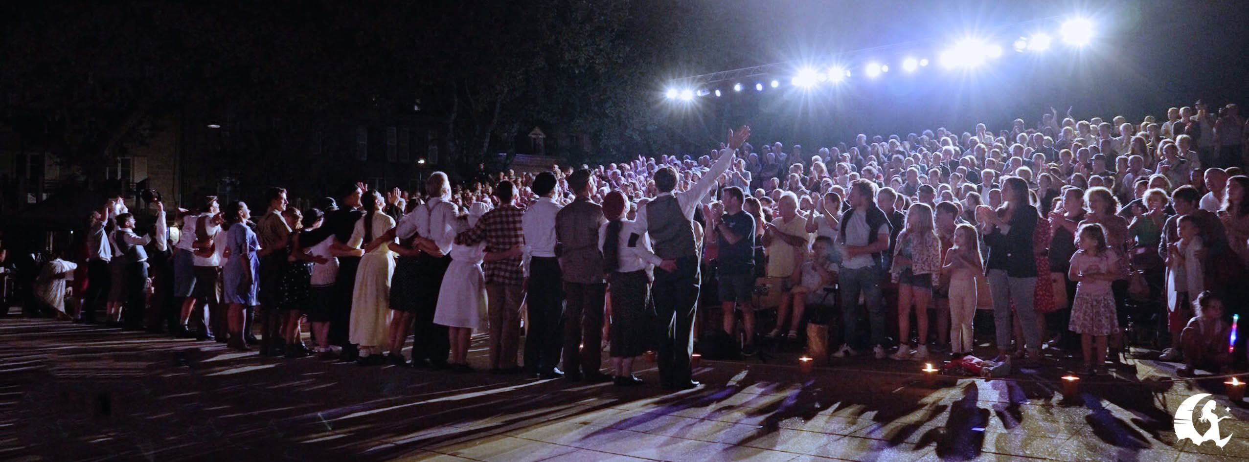 Plusieurs comédiens se tenant mains dans la mains sur un fond de chateau illuminés par des feux d'artifices