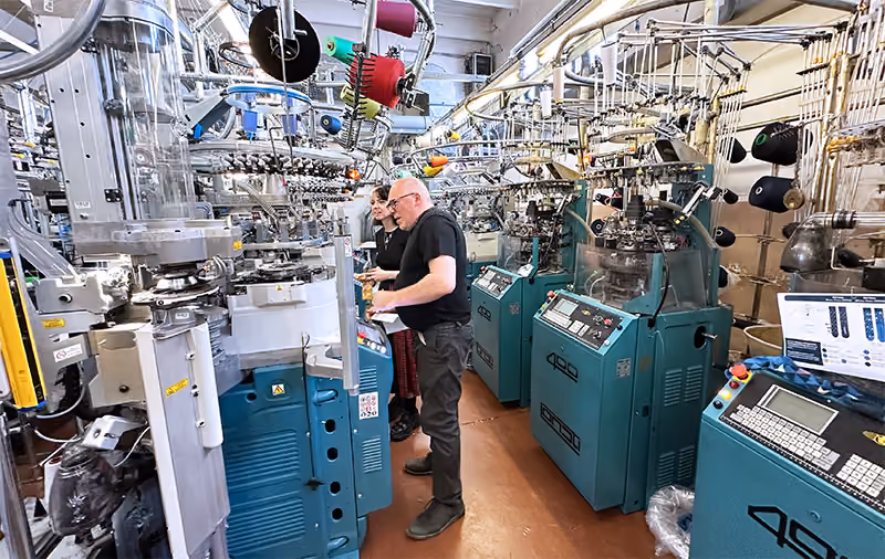 Industrial textile machine workshop with workers operating complex knitting machinery