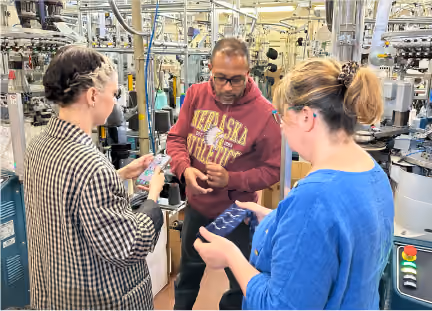 Three workers discuss product in industrial manufacturing facility