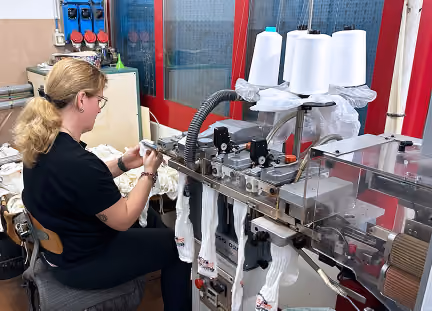 Woman operating industrial textile machine with large spools of white thread