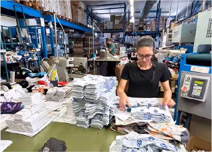 Worker sorting printed fabric in busy textile manufacturing warehouse