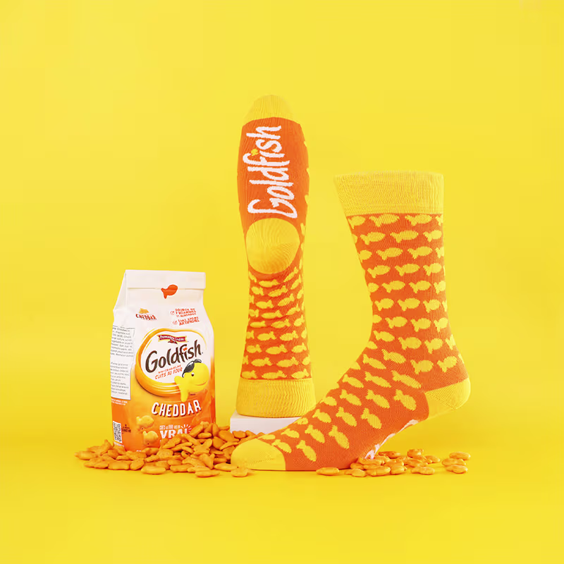 Pair of custom orange and yellow socks with goldfish patterns next to a bag of Cheddar Goldfish crackers.