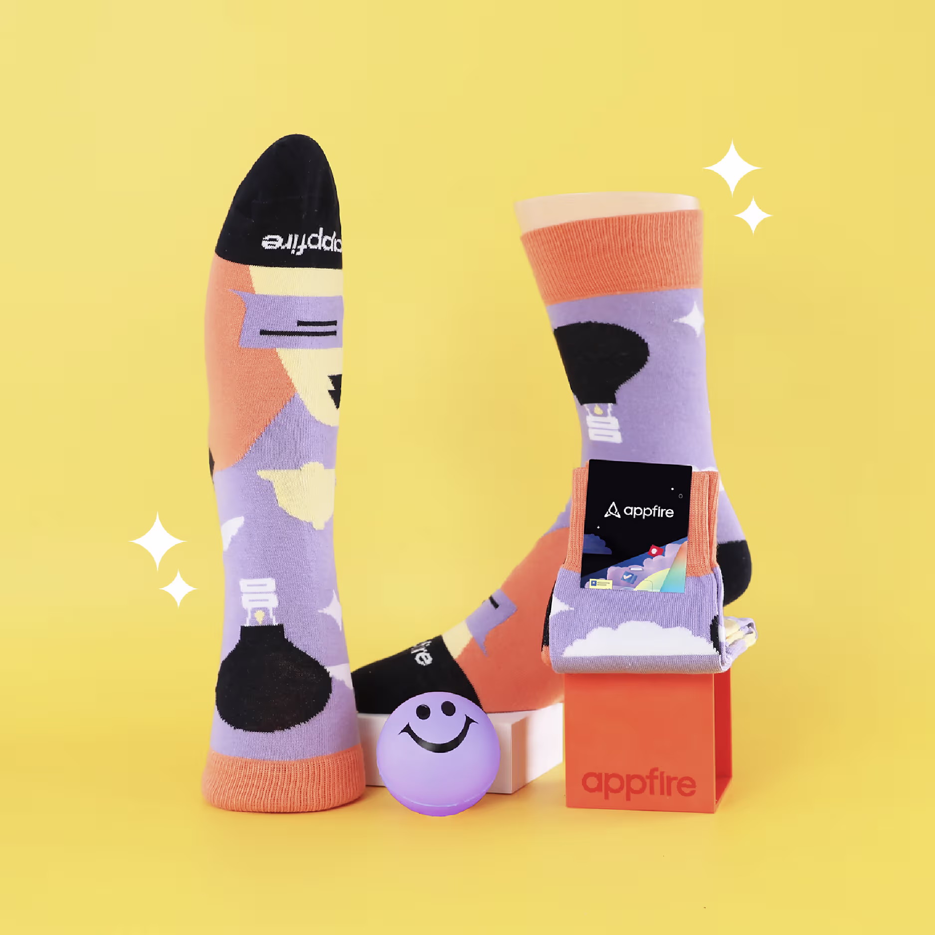 Purple and orange socks with lightbulb design displayed on yellow background with appfire logo box and smiley ball.