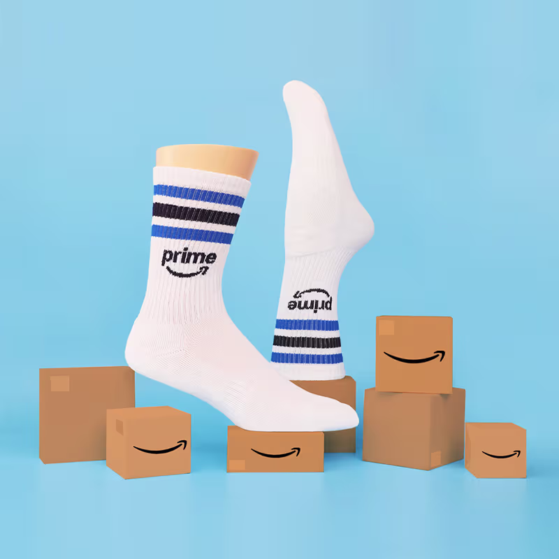 Pair of custom white socks with blue, black stripes and Amazon Prime logo surrounded by Amazon boxes on blue background.