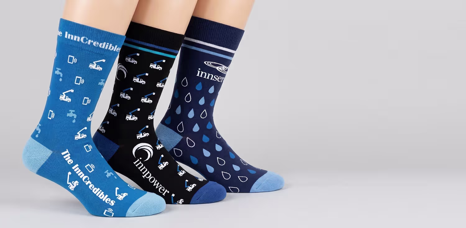Three pairs of custom InnMedia branded crew socks in blue, black and navy