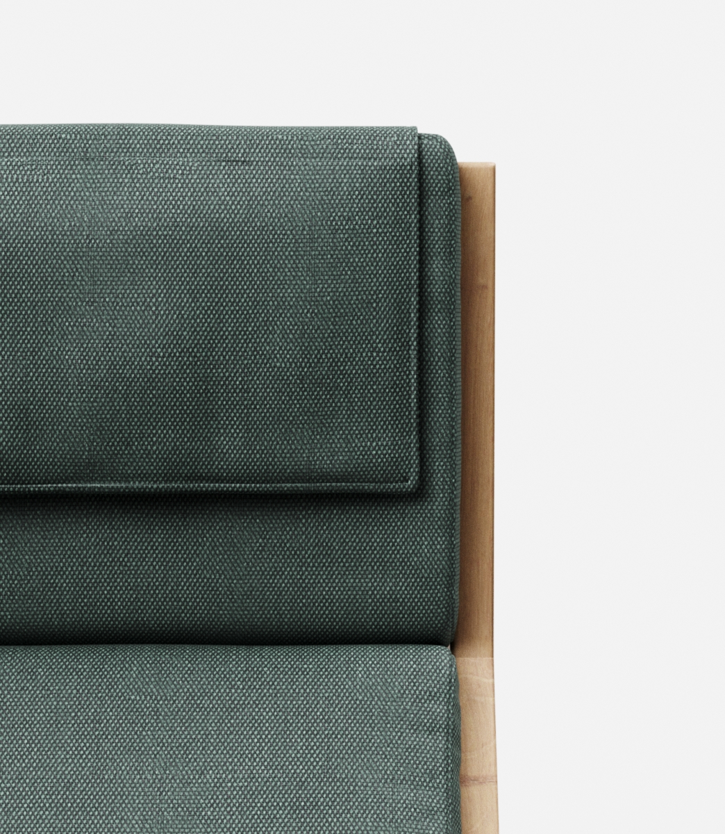 Detail van een bank met groen gestoffeerde kussens en een houten frame aan de rechterkant.