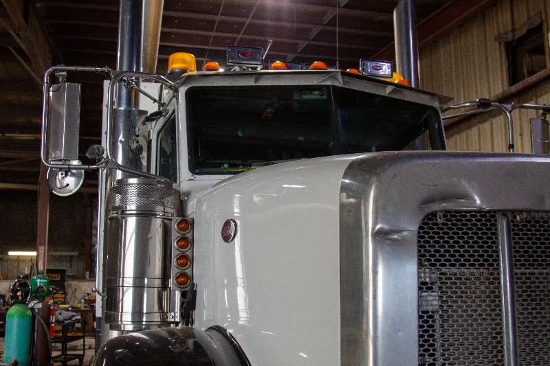 Collision repair on a heavy-duty truck with a dented grille parked inside a maintenance shop.