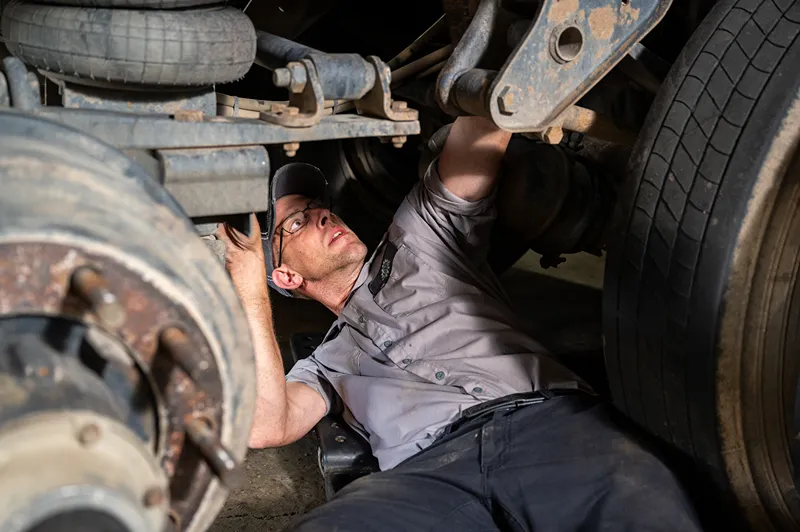 DOT inspection of a heavy-duty truck suspension by a technician checking undercarriage components.