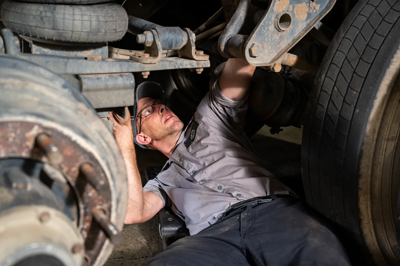 DOT inspection of a heavy-duty truck suspension by a technician checking undercarriage components.
