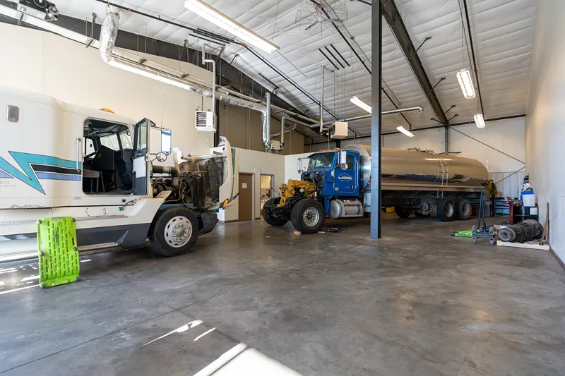 Long Prairie Work Trucks undergoing heavy-duty repair in a spacious shop, including a tanker truck with its hood open.