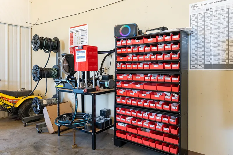 Organized red bins of heavy-duty truck replacement parts beside hydraulic hose equipment, Gates charts, and a Tri-Moto 125.