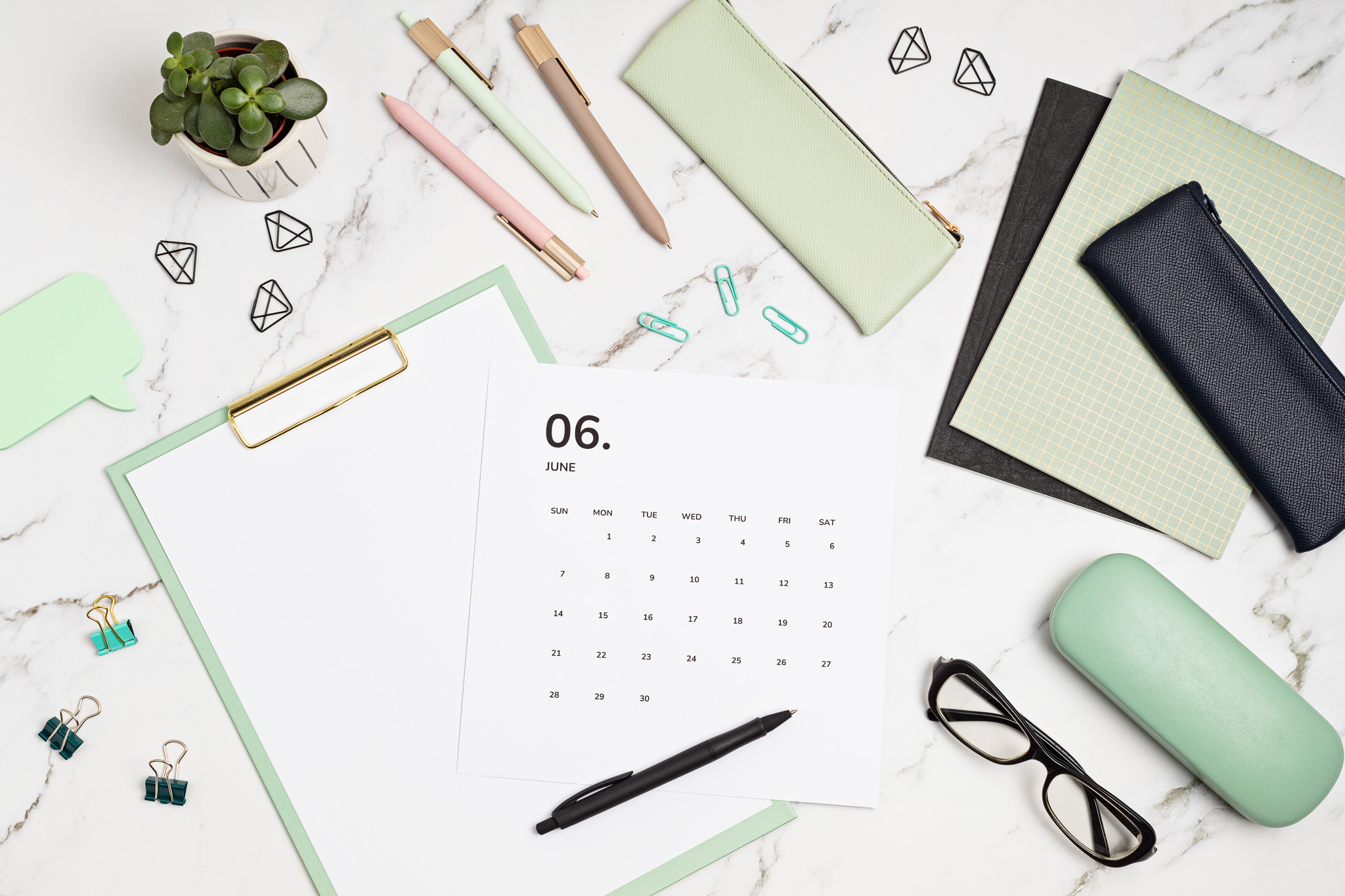 This image shows a marble desk with pens, glasses, a calendar and other office materials.
