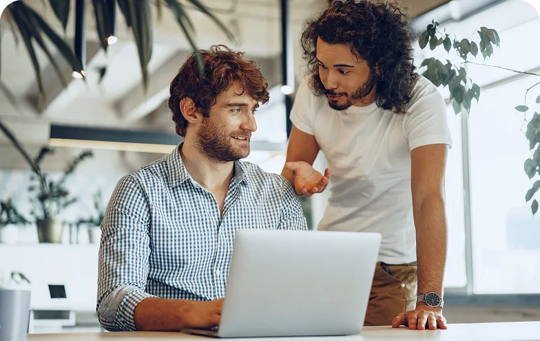 Two men discussing something while working together on a laptop in a modern office.