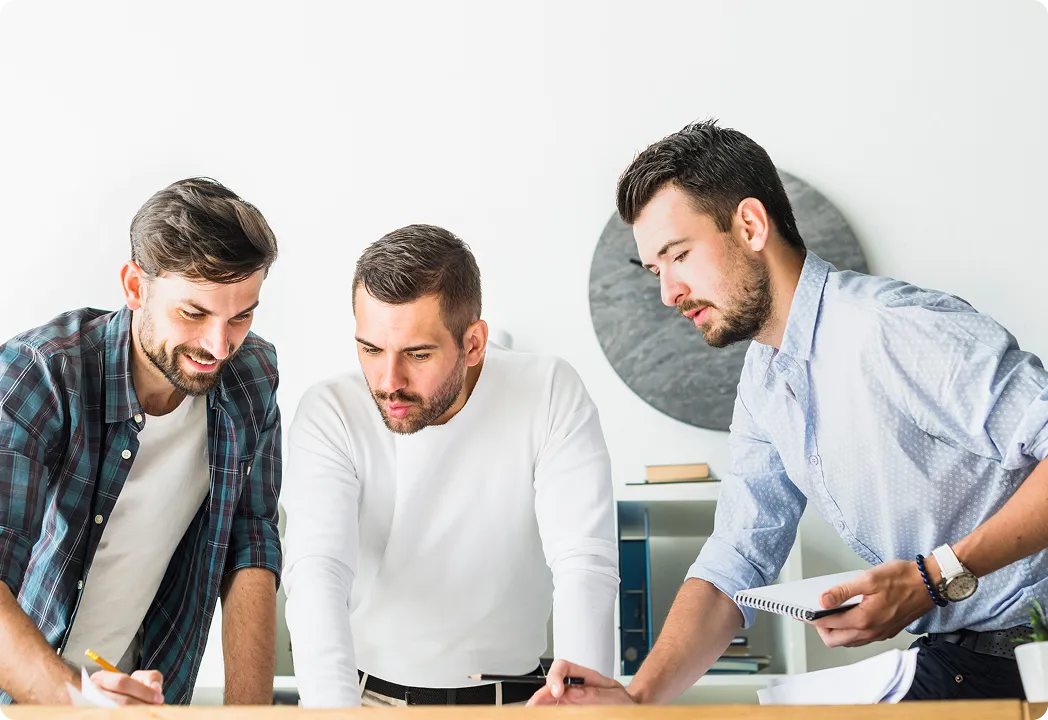 hree men collaborating at a table, writing and discussing something in a marketing agency.
