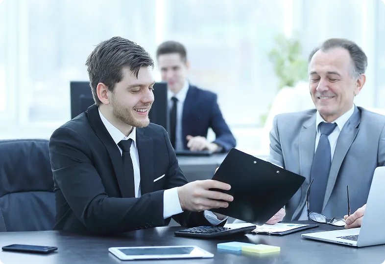 Virtual assistant in a headset and suit smiling while using a laptop in a bright office setting.