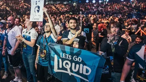 Team Liquid fans cheering at an esports event with a large flag.