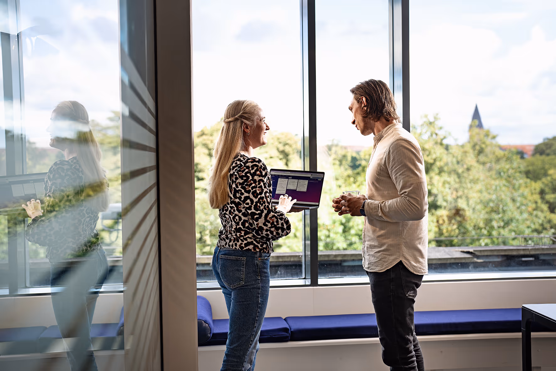 Two Monthio colleagues look over Copenhagen office while holding a coffee and laptop