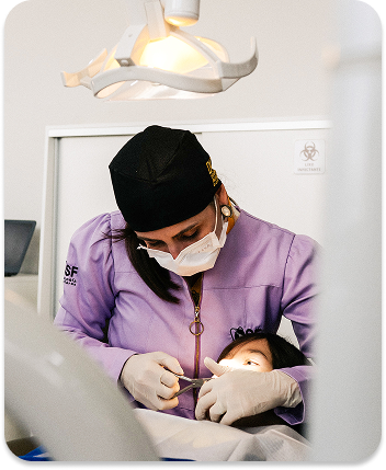 Two dentists wearing white coats, hair covers, masks, and glasses attending to patients in a dental clinic setting.